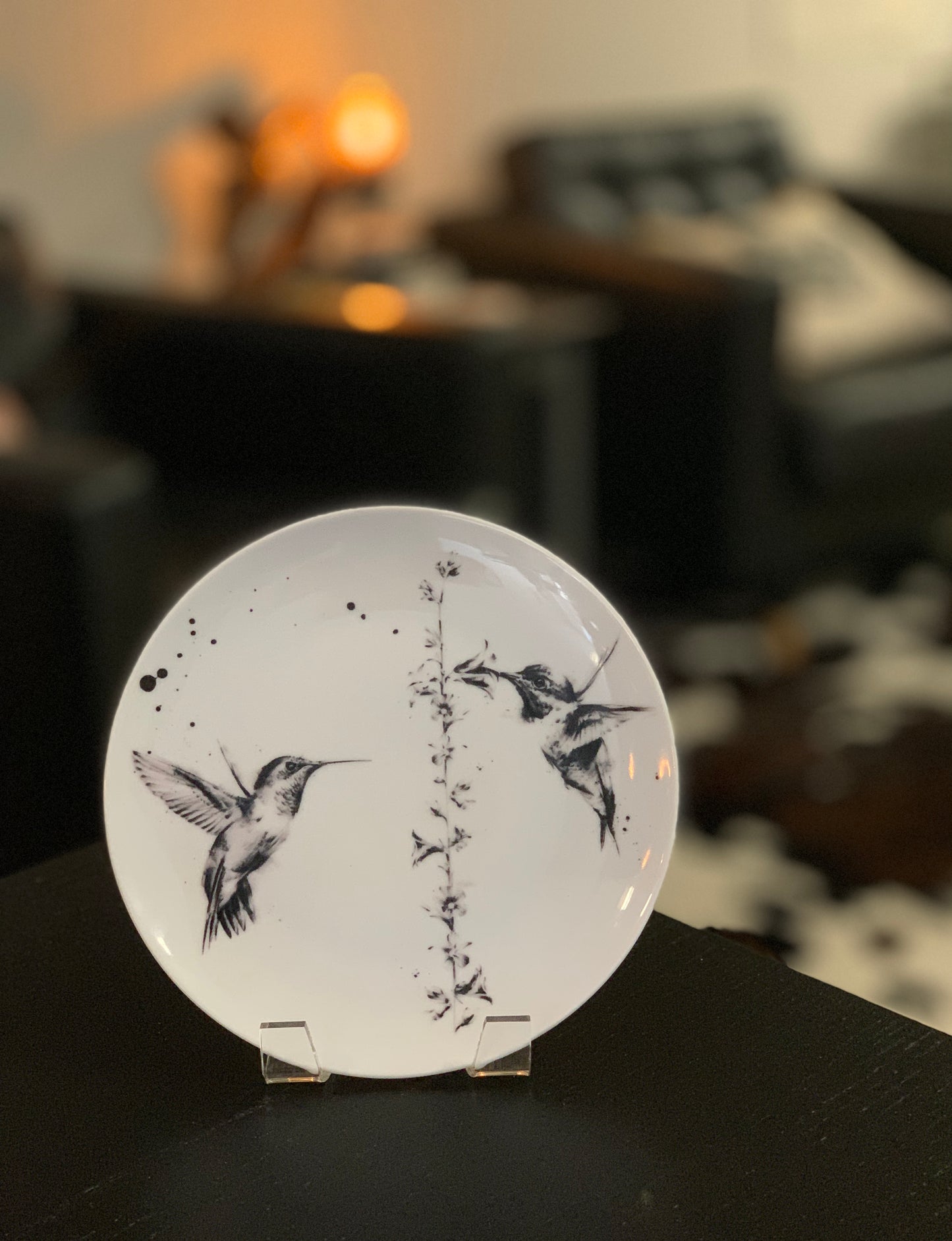 White coupe dinner plate printed with 2 black and grey hummingbirds and a flower, on a table in a home setting