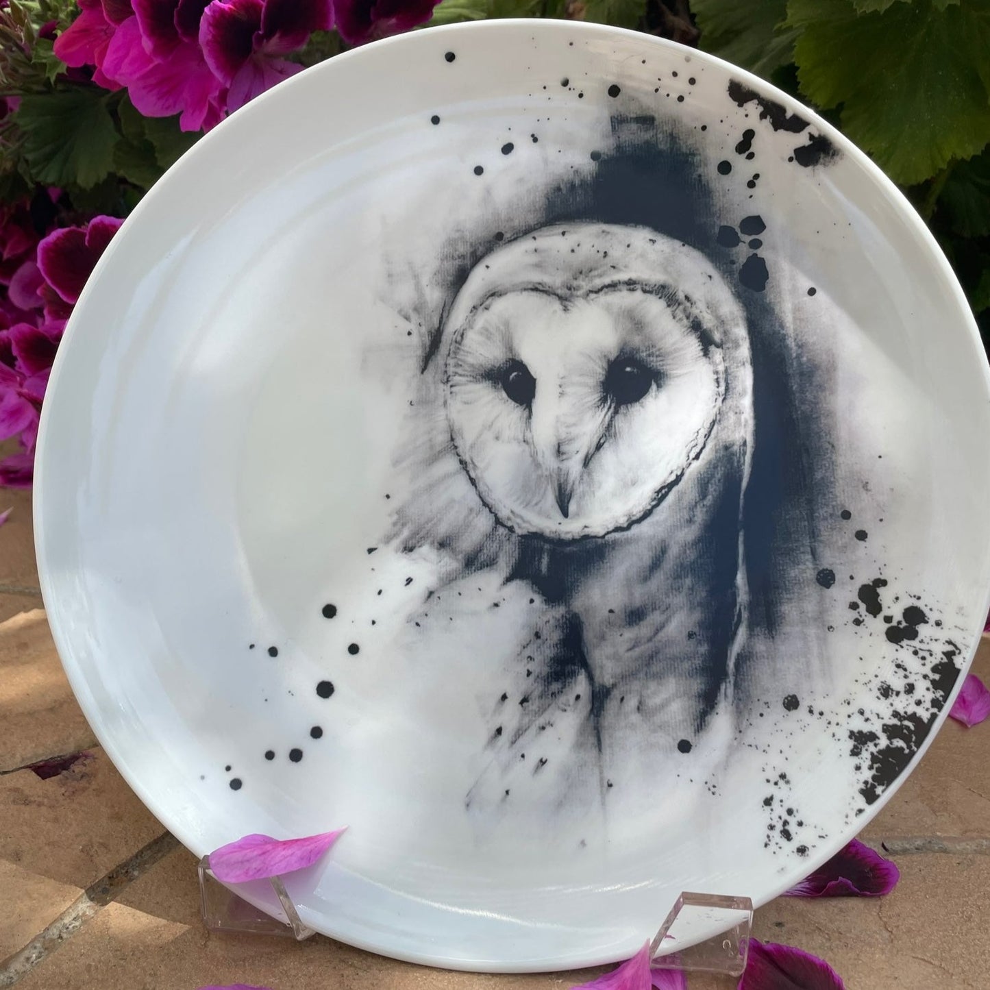 Printed Barn owl dinner plate displayed outside in garden with pink flowers