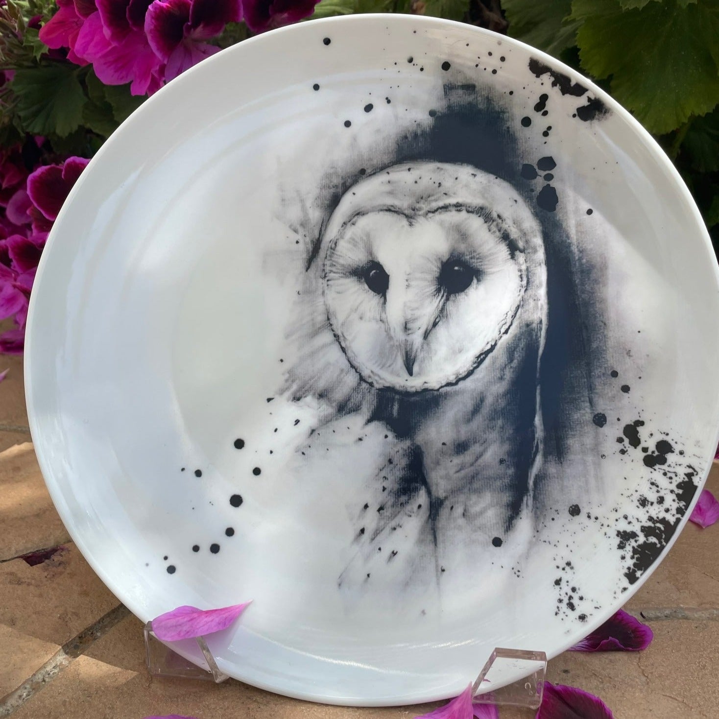 Printed Barn owl dinner plate displayed outside in garden with pink flowers