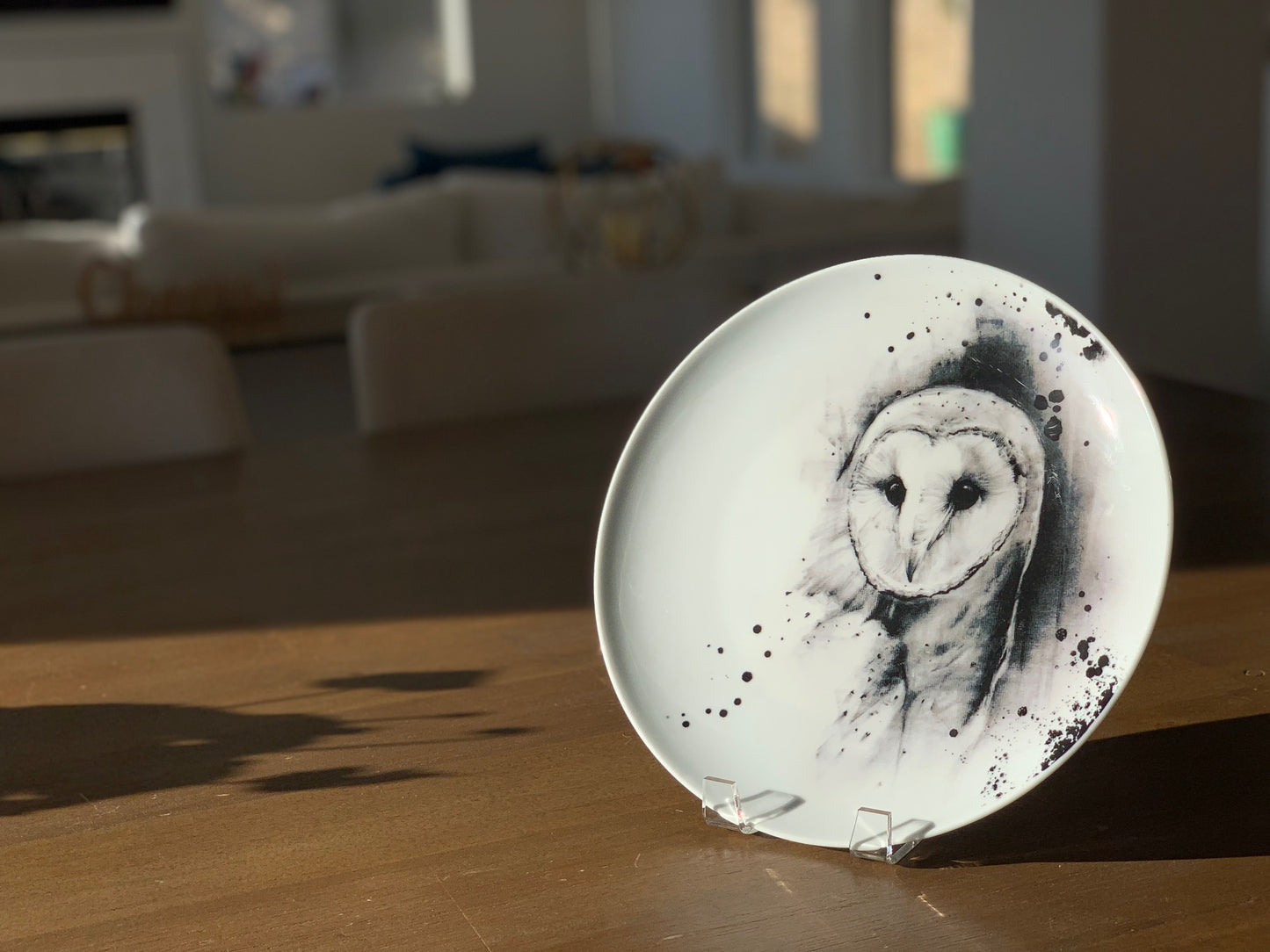 White coupe dinner plate decorated with black and white barn owl, displayed on wood table in dining room of upscale home.